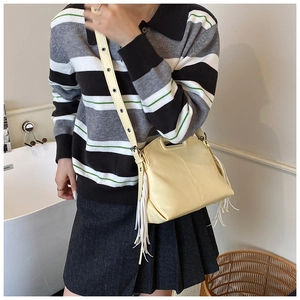Detail of a beige fringe crossbody bag with top handle and adjustable eyelet strap