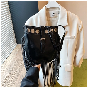 Detail of black crossbody bucket bag with metal rivets and long bohemian fringe