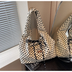 Close-up of polka dot canvas tote featuring a decorative bow and brown leather logo tag