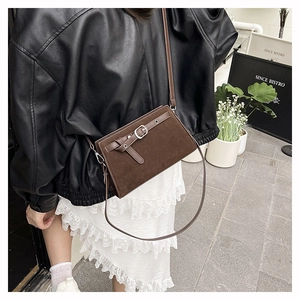 Petit sac bandoulière marron en daim avec boucle porté avec une veste en cuir noir chic