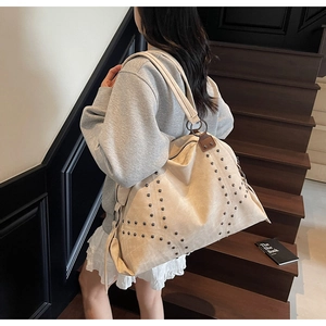 Detail view of beige canvas tote bag with studs worn by a model on stairs