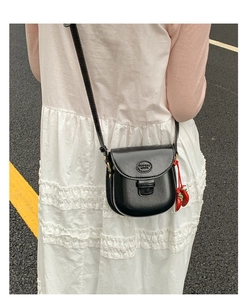 Side view of a vintage black leather saddle bag with a cute red strawberry charm