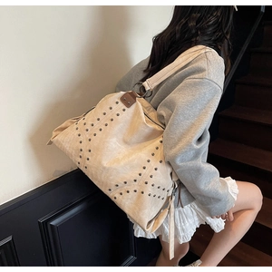 Close-up of beige canvas tote bag featuring metallic rivets and leather strap details
