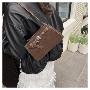 Gros plan sur la texture en daim marron foncé mat et la boucle en métal argenté du sac