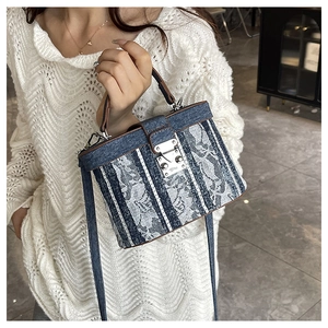 Detail of square denim handbag with white lace floral applique and silver metal buckle