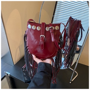 Detail of dark red fringe bucket bag with metallic rivets and polished leather texture