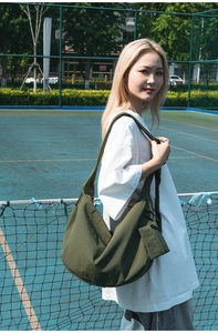 Detail of army green nylon dumpling bag with mini pouch on a model in a tennis court