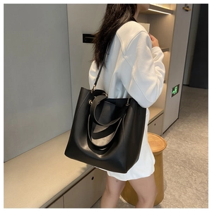 Detail of minimalist black matte leather tote bag worn by model in modern interior