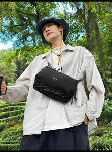 Detail of black nylon crossbody bag with drawstring and brand logo in forest setting