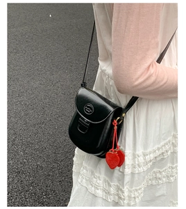 Detail of a black mini saddle bag with metal buckle and a red strawberry charm