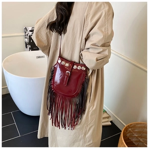 Detail of a dark red patent leather bucket bag with silver rivets and long hanging tassels