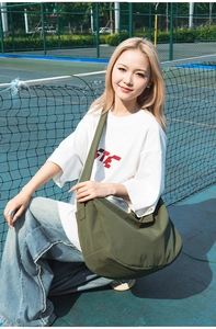 Detail of olive green nylon dumpling bag with wide shoulder strap in outdoor tennis setting