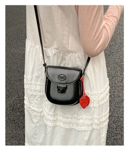 Detail of black saddle bag with a decorative red strawberry charm and embossed logo