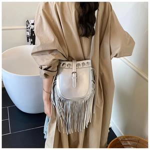 Detailed view of silver fringed crossbody bag with metal studs worn over a trench coat