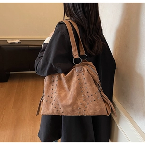 Detail of studded dark brown tote bag with large metal ring handles on model back