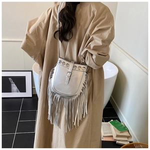 Detail of silver metallic bucket bag with fringe and rivets worn by a model in a stylish room