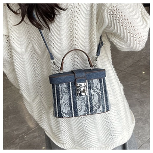 Detail of a white lace and denim mini bucket bag with a brown handle and silver lock