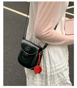 Detail of black faux leather crossbody saddle bag with cute red strawberry charms