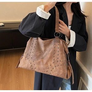 Detailed close-up of brown suede tote bag featuring vintage metal rivets and distressed texture
