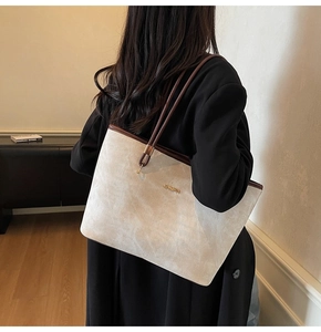 Detail of a large cream tote bag with dark brown straps worn by a model in a home setting