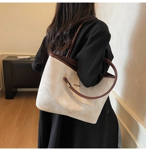 Rear view of a cream and brown leather tote bag worn by a model in a warm setting