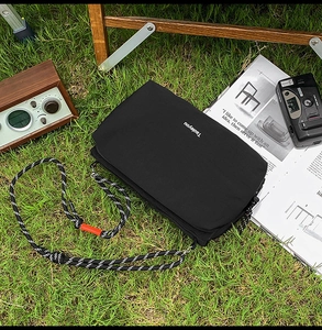 Detail of black canvas crossbody bag with orange clip on rope strap over grass background