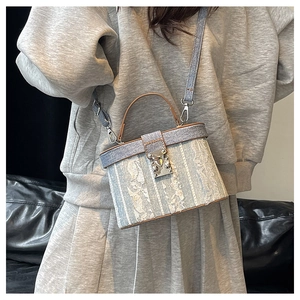 Detail of light blue denim box bag with white lace trim and brown leather handle