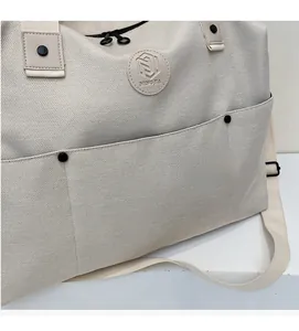 Close-up of cream canvas travel bag with large front pocket and embossed leather logo