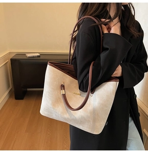 Macro view of beige tote bag with brown leather trim and golden metal logo detail