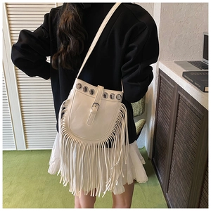 Close-up of white tassel crossbody bag with metallic grommets and bohemian fringe detail