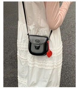 Detail shot of a black saddle crossbody bag with heart charms on a white pleated dress