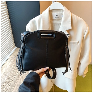 Detail of black leather tote bag featuring side tassels and integrated hollow handle design