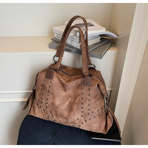 Close-up of vintage brown tote bag featuring decorative metal rivets and wide shoulder strap