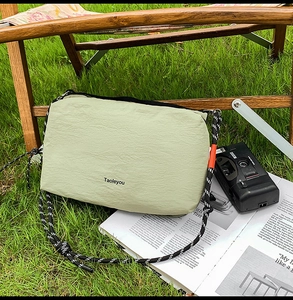 Detail of green nylon crossbody bag with woven rope strap on a wooden chair