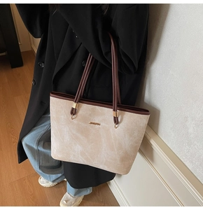 Detail of minimalist beige suede tote bag showing smooth leather straps and metal logo