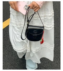 Close-up of a black leather saddle bag with a cute strawberry charm and long strap