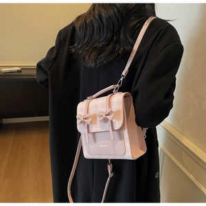 Dettaglio dello zaino rosa a quadretti con fiocchi indossato su un blazer nero