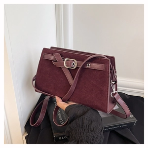 Gros plan sur la texture en daim mat bordeaux et le détail de la sangle en cuir du sac