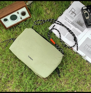Detail of light green waterproof crossbody bag with woven rope strap on grass