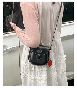 Mini black leather saddle bag with strawberry charm accessory on a model outdoors
