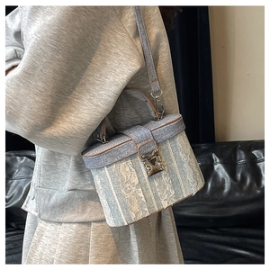 Detail of blue denim bucket bag featuring white floral lace overlay and leather trim
