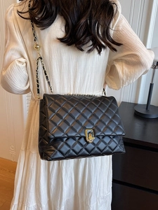 Elegant black quilted chain bag with gold buckle worn by a model in a white dress