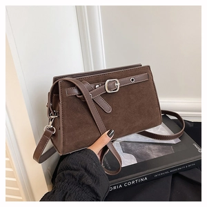 Gros plan du sac bandoulière en daim marron avec boucle décorative posé sur un livre