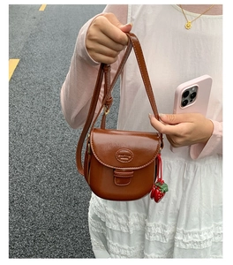 Detail of a brown vintage saddle bag with strawberry charm and adjustable strap