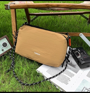 Detail of khaki nylon crossbody bag with woven strap on outdoor camping grass setting