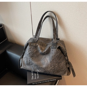 Detail of vintage grey leather tote bag featuring stylish rivet studs on a black leather chair