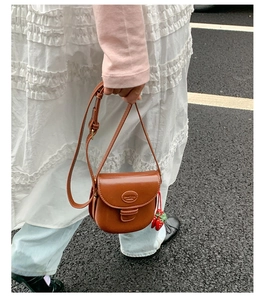 Retro brown saddle bag with matte leather and cute strawberry charm on a street setting