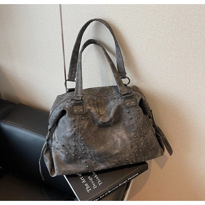 Close-up of vintage washed leather tote bag with dark metal rivets on a leather sofa