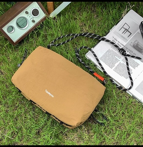 Close-up of khaki nylon hiking crossbody bag with woven rope strap on a grassy lawn