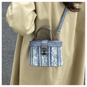 Detail of denim blue lace bucket bag with brown leather handle on a khaki trench coat